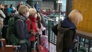 Bahnreisende warten im Hamburger Bahnhof. Viele haben ihre Koffer mit dabei. Einigetragen eine Mund-Nasen-Bedeckung. © Screenshot 