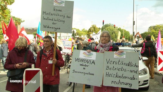 Demonstrierende halten Schilder hoch, mit denen sie gegen steigende Mieten, für eine Verstaatlichung von Vonovia und für verständliche Nebenkostenabrechnungen sind. © Screenshot 