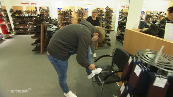 Ein junger Mann probiert Turnschuhe im Schuhgeschäft an. © Screenshot 