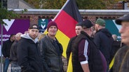 Männer mit einer Deutschlandfahne stehen auf einem Platz. © Screenshot 
