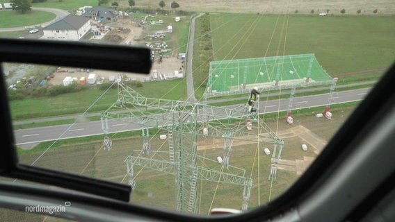 Der Blick aus einem Hubschrauber auf einen Arbeiter der eine Stromtrasse verlegt. © Screenshot 