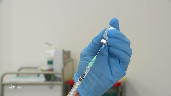 Zwei Hände in Latexhandschuhen ziehen eines Impfspritze aus einer Ampulle auf. © Screenshot 