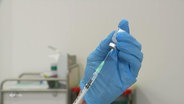 Zwei Hände in Latexhandschuhen ziehen eines Impfspritze aus einer Ampulle auf. © Screenshot 