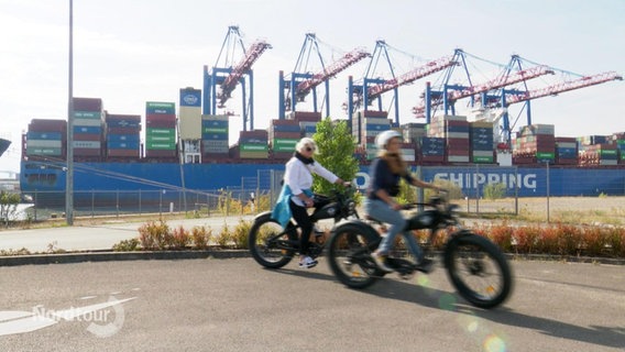 Radfahrer vor einem Containerschiff. © Screenshot 