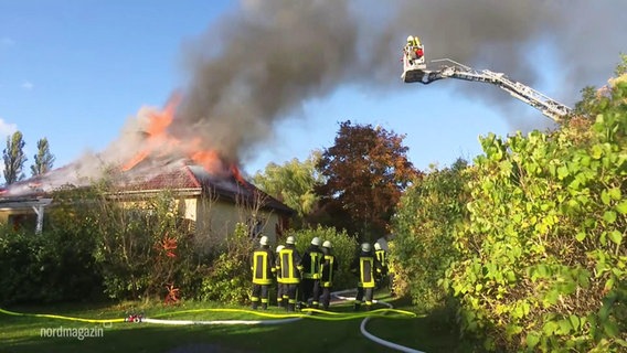 Ein Dachstuhl eines Hauses steht in Flammen. Ein Feuerwehrmann löscht ihn von einer Drehleiter aus. © Screenshot 