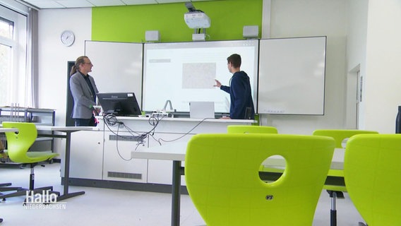 Ein Lehrer und ein Schüler stehen an einer Tafel in einem Klassenzimmer. © Screenshot 