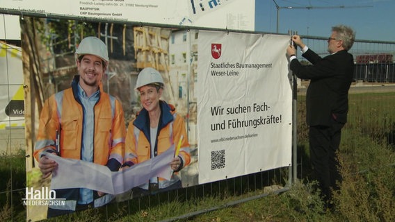 Ein Mann befestigt ein Plakat an einem Bauzaun. © Screenshot 