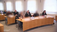 Beteiligte eines Prozesses sitzen in einem Gerichtssaal. © Screenshot 