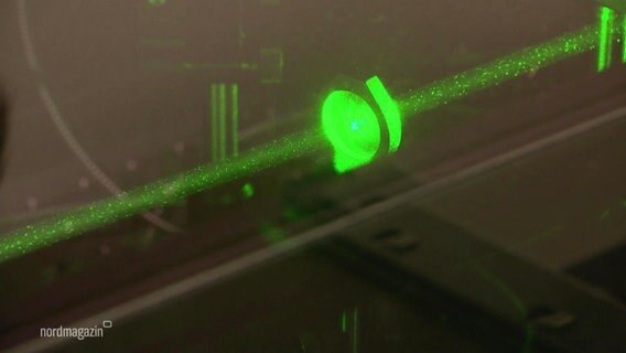 Kleine Teilchen schweben in einem grünen Laserstrahl. © Screenshot 