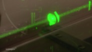 Kleine Teilchen schweben in einem grünen Laserstrahl. © Screenshot 