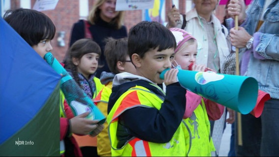 Kinder halten sich beim Sprach-Kita Protesten Papierröhren vor die Münder. © Screenshot 