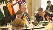 Bundeswirtschaftsminister Robert Habeck und Bundesfinanzminister Christian Lindner beugen sich vor dem niedersächsischen Ministerpräsidenten Stephan Weil zueinander, um etwas zu besprechen. © Screenshot 