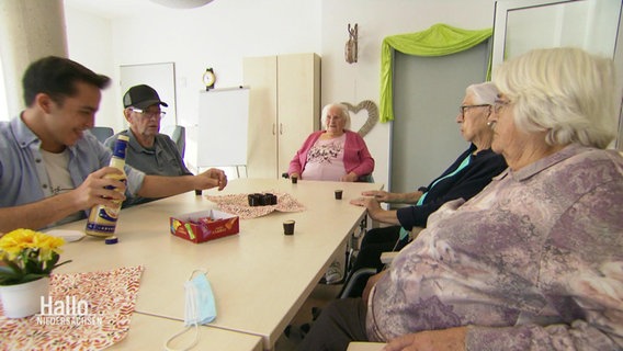 An einem Tisch in einem Seniorenheim sitzen mehrere ältere Herrschaften und ein Pfleger beisammen. © Screenshot 