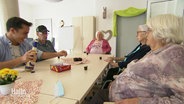 An einem Tisch in einem Seniorenheim sitzen mehrere ältere Herrschaften und ein Pfleger beisammen. © Screenshot 