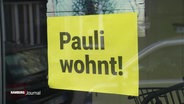 In einem Fenster hängt ein gelber Zettel mit der Aufschrift: "Pauli wohnt!" © Screenshot 