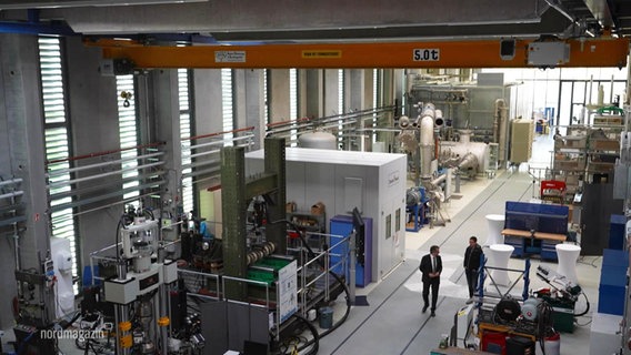 In einer Halle stehen mehrere große Maschinen und Geräte zu Forschungszwecken. © Screenshot 