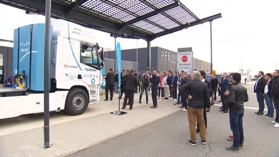 Mehrere Journalistinnen und Journalisten stehen an einer Wasserstoff-Tankstelle, an der ein Lkw hält. © Screenshot 