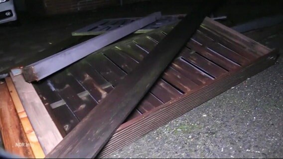 Auf Aspahltboden liegt das Geländer eines Holzbalkons. © Screenshot 