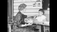 Ein Schwarz-Weiß-Foto zeigt, wie eine Frau einem gehörlosen Kind das sprechen beibringen will. © Screenshot 