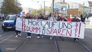 Protestierende halten einBanner mit der Auzfschrift: "Hört auf uns dumm zu sparen" © Screenshot 