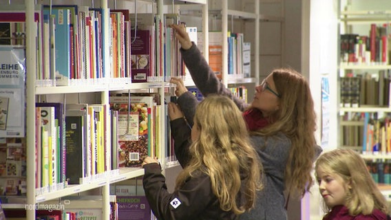 Eine Mutter und ihre beiden Töchter stöbern in einer Bibliothek © Screenshot 