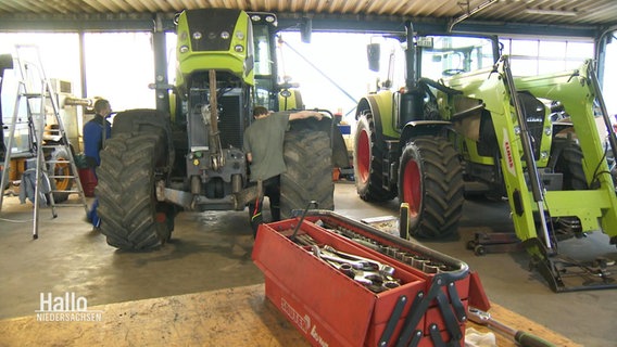 Zwei Trecker stehen in einer Waagenhalle. Davor steht eine Werkzeugkiste. © Screenshot 