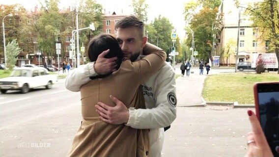 Eine Frau und ein Mann umarmen sich auf einer Straße. © Screenshot 