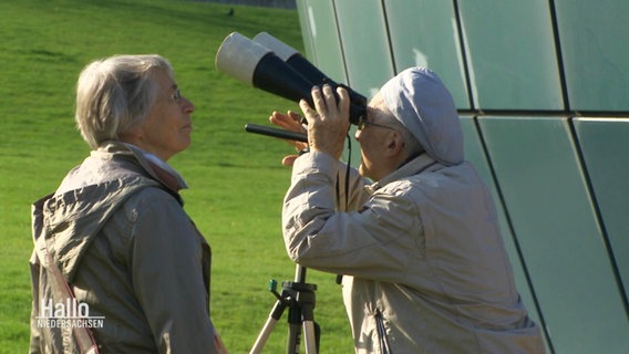 Zwei Personen betrachten die partielle Sonnenfinsternis durch ein Teleskop. © Screenshot 