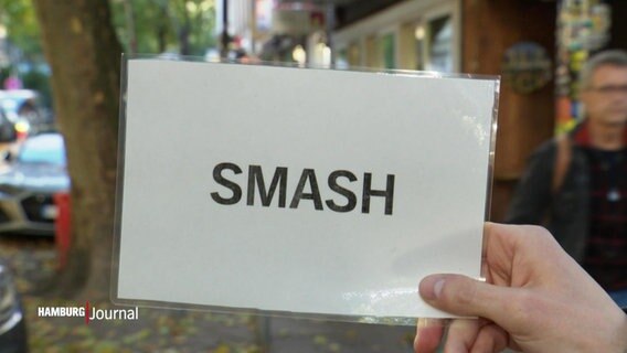 Eine Hand hält einen Zettel mit der Aufschrift "Smash" in die Kamera. © Screenshot 