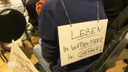 Ein Schild auf dem Rücken einer Person warnt vor Umweltschäden. © Screenshot 