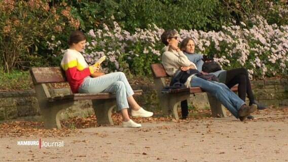 Drei Menschen sitzen auf zwei Bänken in einem Park und halten ihre Gesichter in die Sonne. © Screenshot 