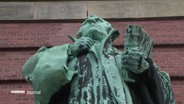 Eine Kupferstatue mit grüner Patina von Martin Luther, die an der Fassade der St. Michaeliskirche in Hamburg steht. © Screenshot 