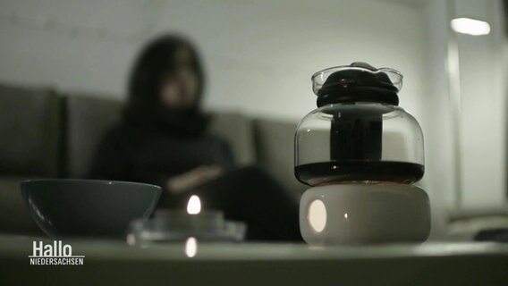 Eine unkenntlich gemachte Frau gibt ein Interview, im Vordergrund eine Kanne Kaffee auf einem Sofatisch. © Screenshot 