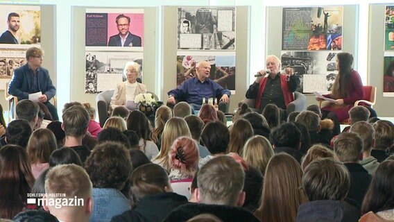 Vier ältere Menschen sitzen auf Podium vor Kindern. © Screenshot 