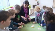 Eine Frau sitzt neben Kindergartenkindern auf dem Boden. Sie spielen gemeinsam ein Spiel. © Screenshot 