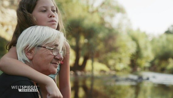 Minja Nikolic steht Arm im Arm mit einer ihrer Enkelinnen an einem Fluss. © Screenshot 