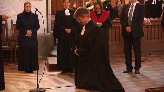 Ein Dompastor kniet auf einer Stufe in einer Kirche. © Screenshot 