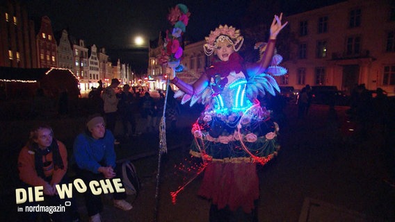 Eine Frau in einem bunt leuchtenden Kostüm. © Screenshot 
