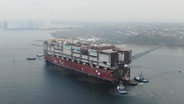 Eine riesige Schiffshälfte die mit offener Außenwand von Schleppern durch einen Hafen gezogen wird © Screenshot 