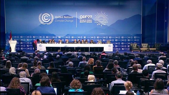 Der Konferenzsaal der Weltklimakonferenz mit zahlreichen Personen auf und vor der Bühne des Saals © Screenshot 
