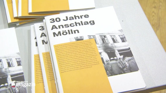 Broschüren mit dem Titel "30 Jahre Anschlag Mölln" liegen auf einem Tisch. © Screenshot 
