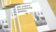 Broschüren mit dem Titel "30 Jahre Anschlag Mölln" liegen auf einem Tisch. © Screenshot 