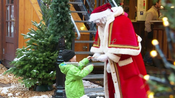 Ein als Weihnachtsmann verkleideter Schausteller überreicht einem kleinen Kind eine Süßigkeit. © Screenshot 