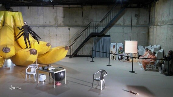 Bühnenbild im Schauspielhaus: ein Mann steht auf einigen sehr großen Bananen. © Screenshot 