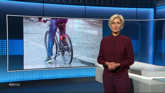 Moderatorin Susanne Stichler steht im NDR Studio vor einem Bildschirm, der einen Fahrradfahrer zeigt. © Screenshot 