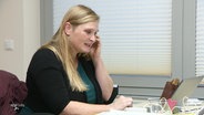 Eine Frau sitzt in einem Büro und spricht in ein Telefon. © Screenshot 