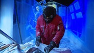 Ein Eiskünstler in Schutzkleidung arbeitet an einem Eisblock. © Screenshot 