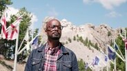 Yared Dibaba steht vor dem Mount Rushmore National Memorial in den USA. © Screenshot 