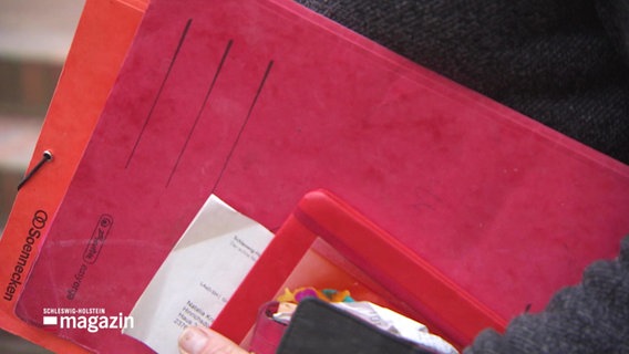 Jemand hält eine Aktenmappe und mehrere Ausweisdokumente in der Hand. © Screenshot 