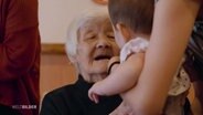 Eine ältere Frau in einem japanischen Altenheim nimmt ein Baby auf den Arm. © Screenshot 